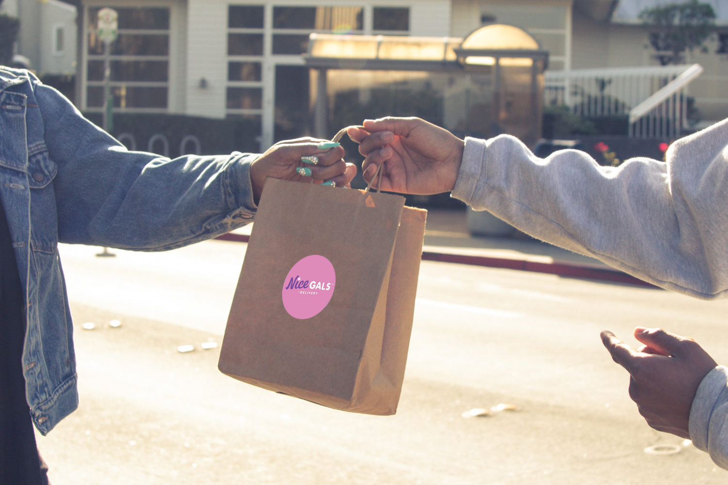 close up of two people handing off a brown paper bag with a sticker for Nice Gals Delivery on it in Marin County, CA